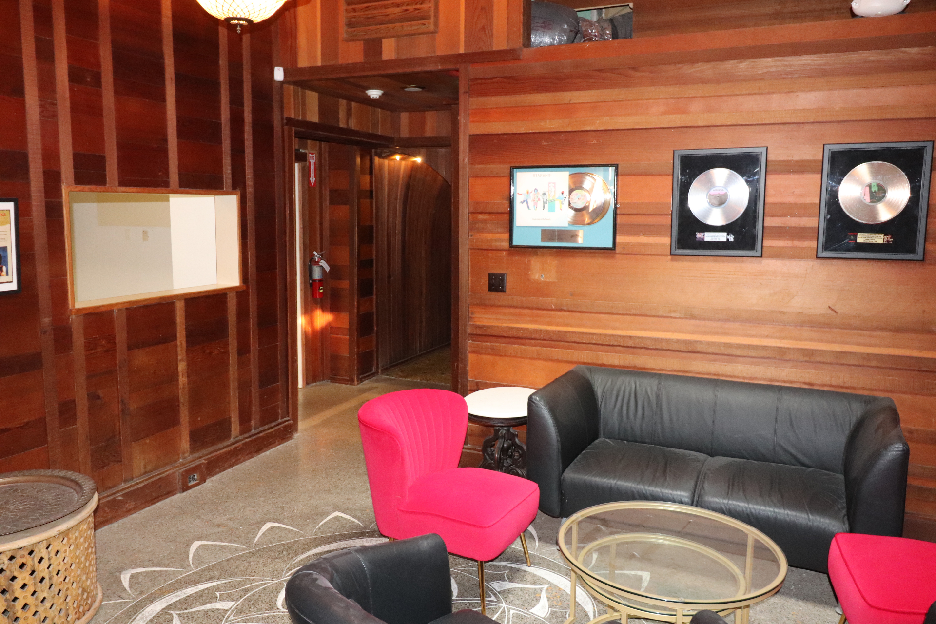Redwood-paneled game room lounge with red velvet chairs, a black leather sofa, and framed gold and platinum records on the wall.