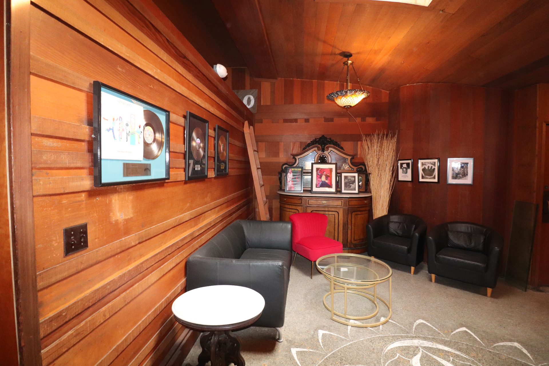 Wider view of the game room with platinum records, framed artist photos, leather seating, and an inlaid sunburst floor.
