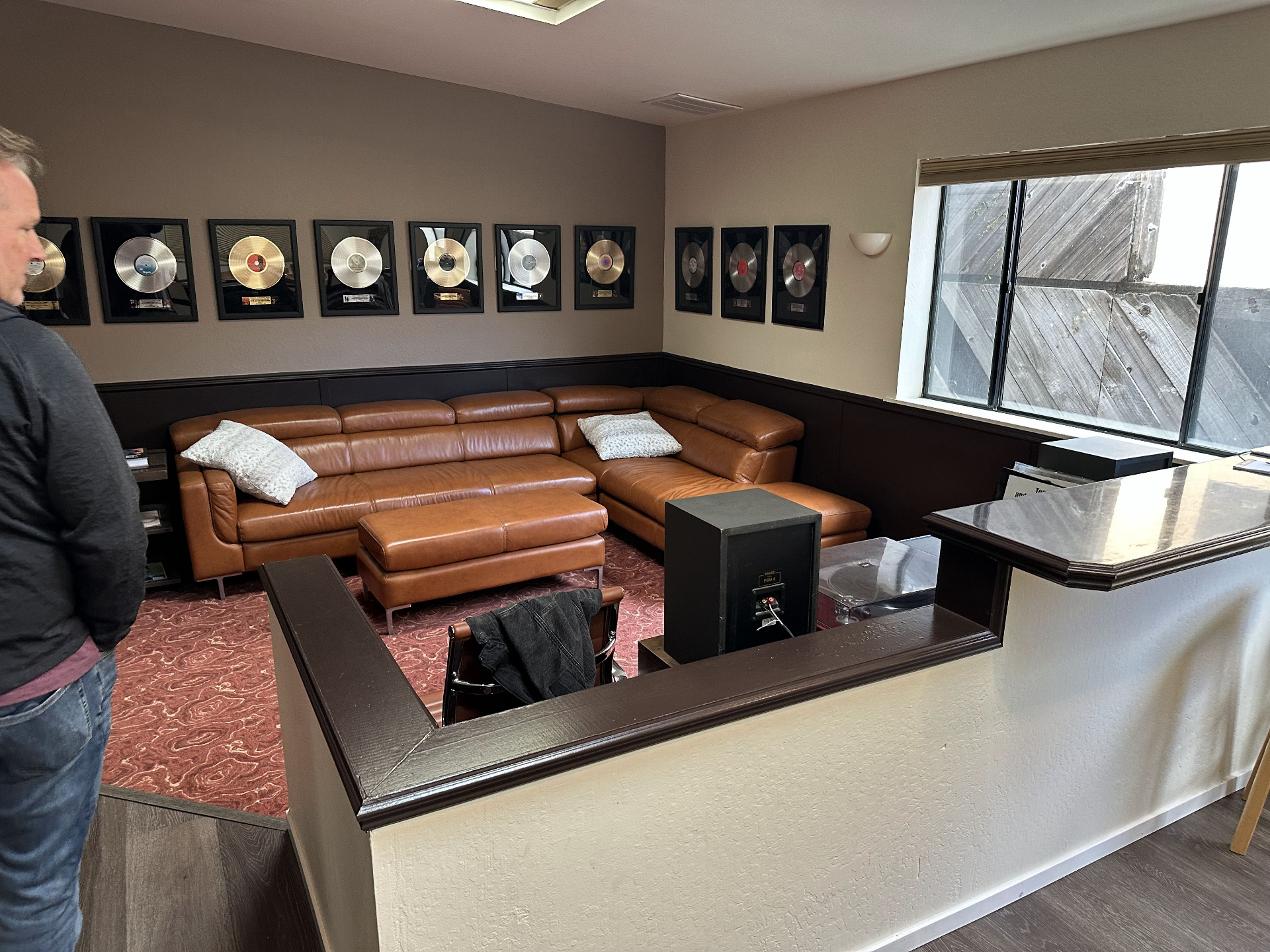 The Metallica Lounge — a tan leather sectional sofa beneath a long row of framed gold and platinum records, with a sunlit window and dark wainscoting.