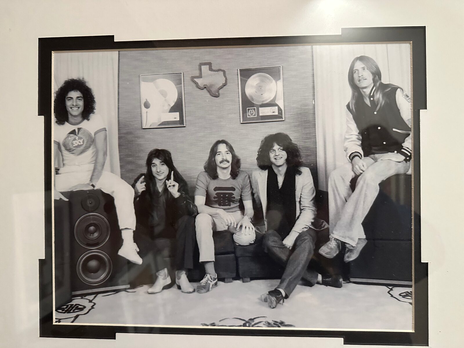 Framed photograph of Journey posing with their RIAA platinum plaques and a Texas state cutout — hanging on the walls of 2200 Studios today.