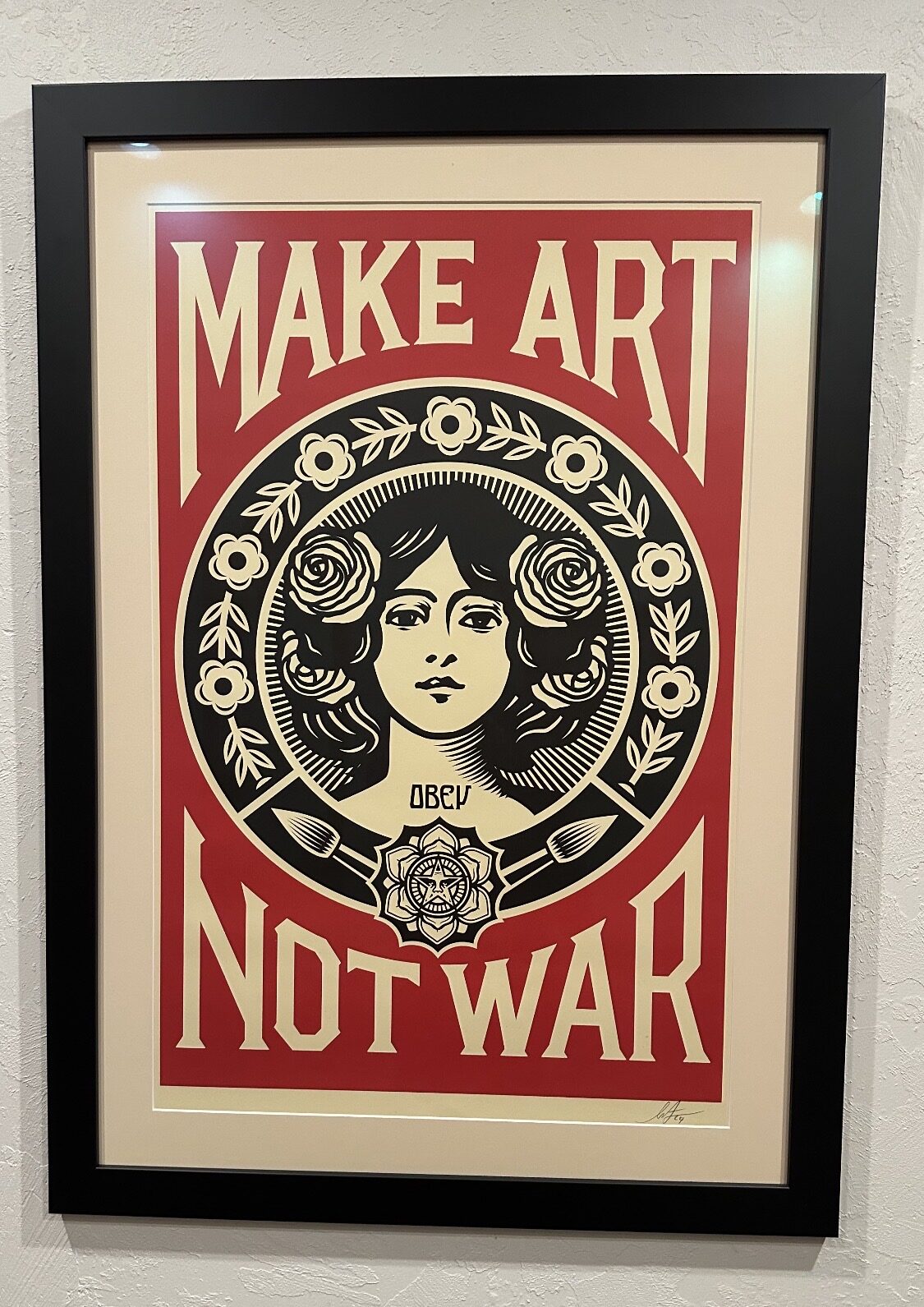 Framed Shepard Fairey 'Make Art Not War' poster — red and cream, woman's portrait flanked by paintbrushes and roses, with the OBEY mandala below.
