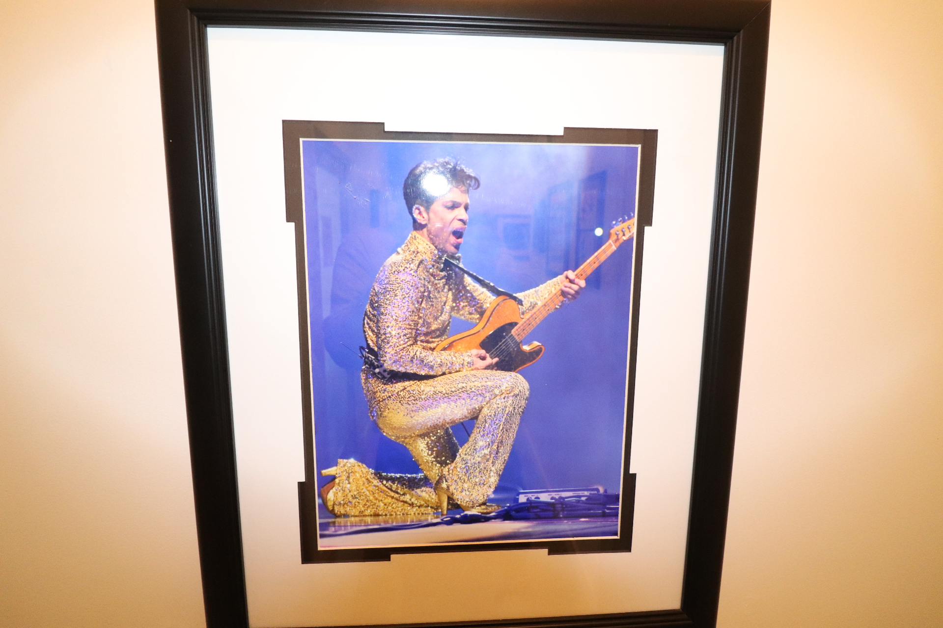 Framed photograph of Prince in a gold sequined suit kneeling with a Telecaster, hanging on a 2200 Studios wall.