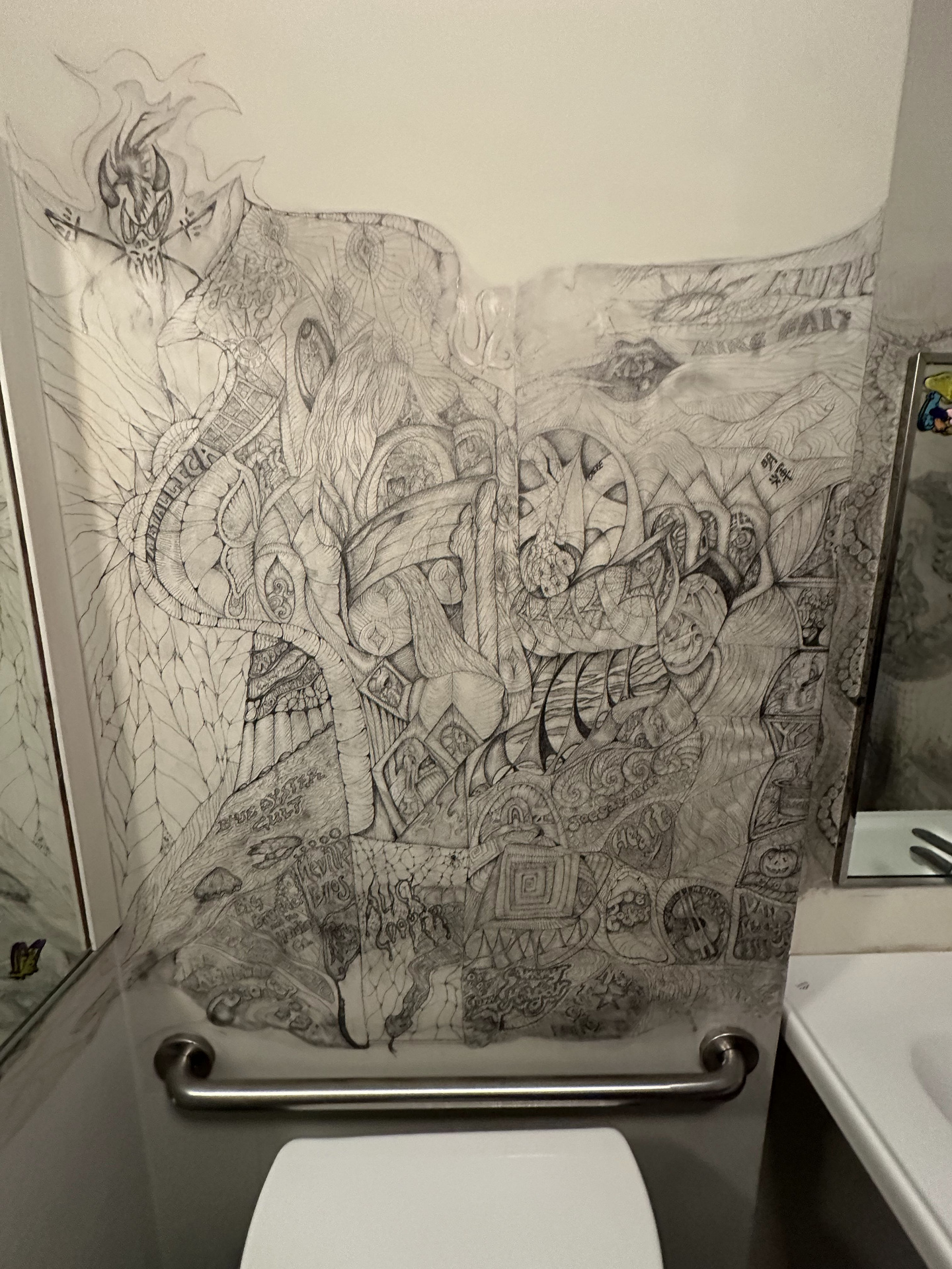 Intricate pencil mural covering a bathroom wall — a flaming demon, dragons, and band names including Metallica, Blue Öyster Cult, and Alice Cooper woven into the design.