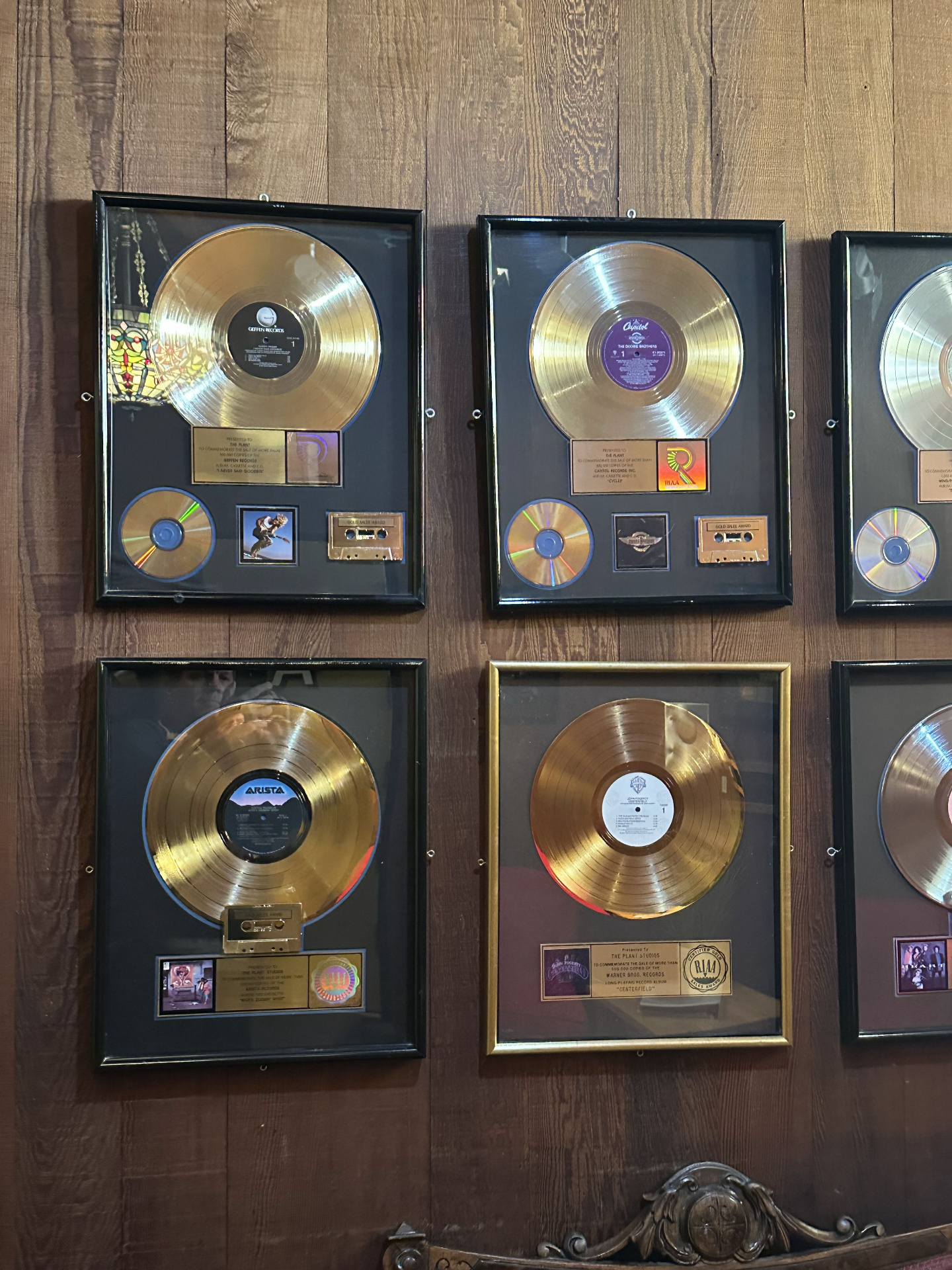 Wall of framed gold and platinum RIAA record awards on redwood paneling — including Doobie Brothers, John Fogerty's Centerfield, and Aretha Franklin's Who's Zoomin' Who.