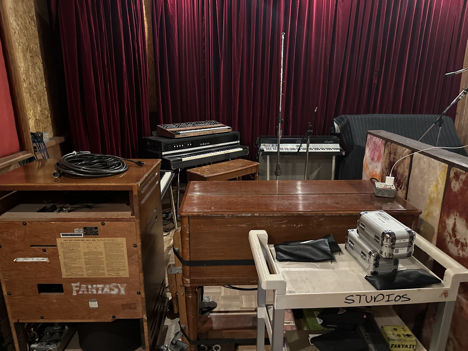 A clutter of vintage keyboards — Yamaha electric piano, Mellotron, Wurlitzer — and a Hammond organ stenciled 'FANTASY' against red velvet curtains.