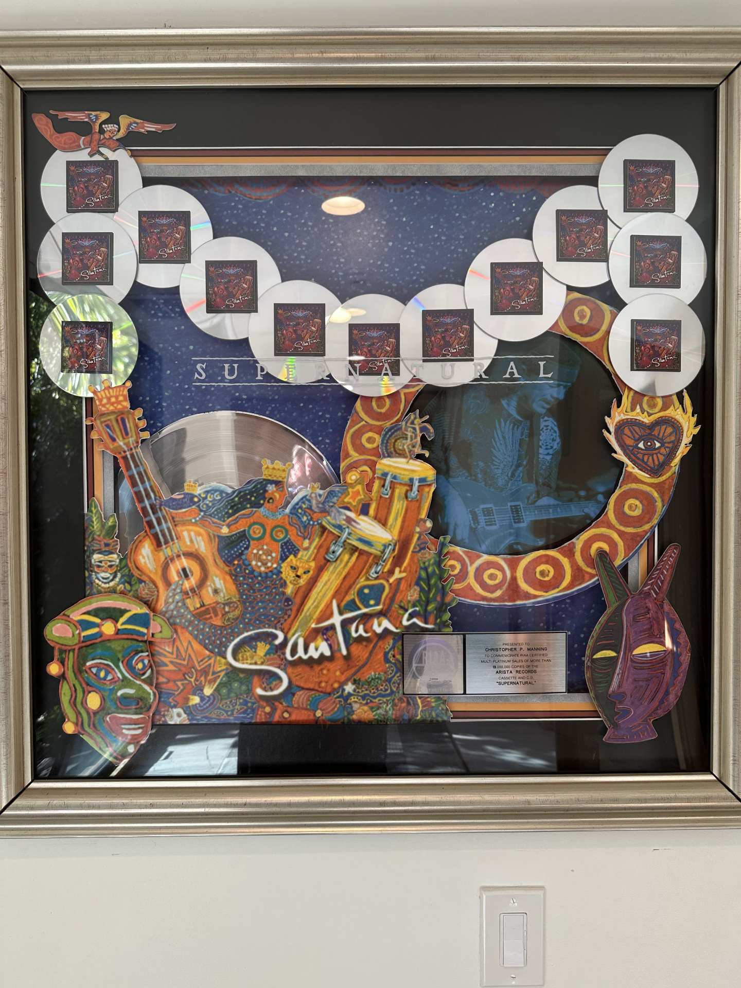 Elaborate framed multi-platinum award for Santana's Supernatural, with cutout discs, masks, and album artwork certifying 13 million copies sold.