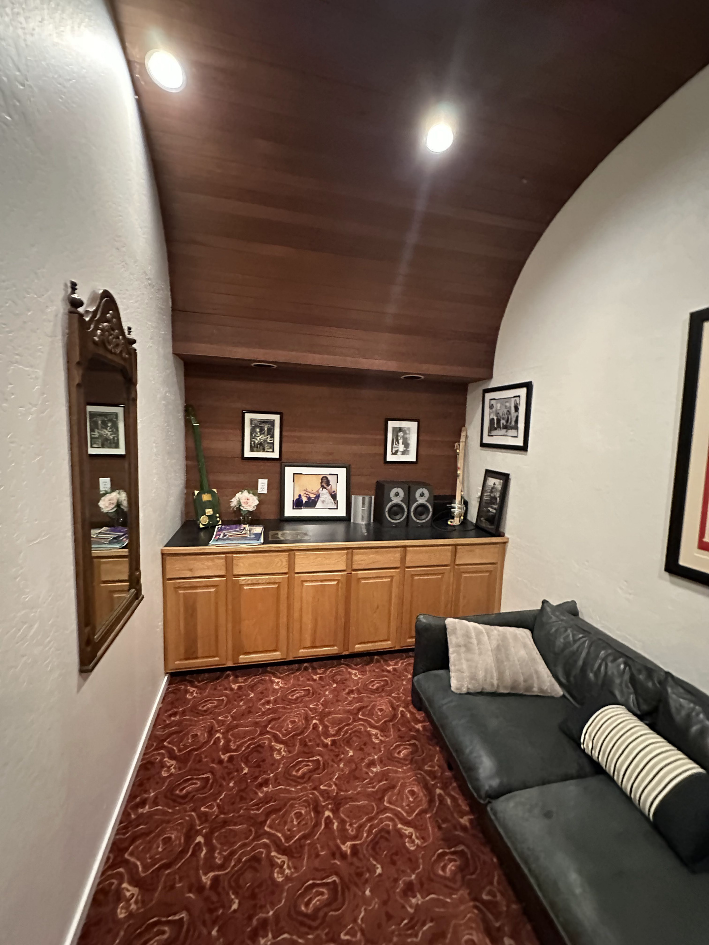 The former Rick James conference room — curved white walls, redwood ceiling, swirling red carpet, a built-in cabinet with framed photos, and a dark sofa.