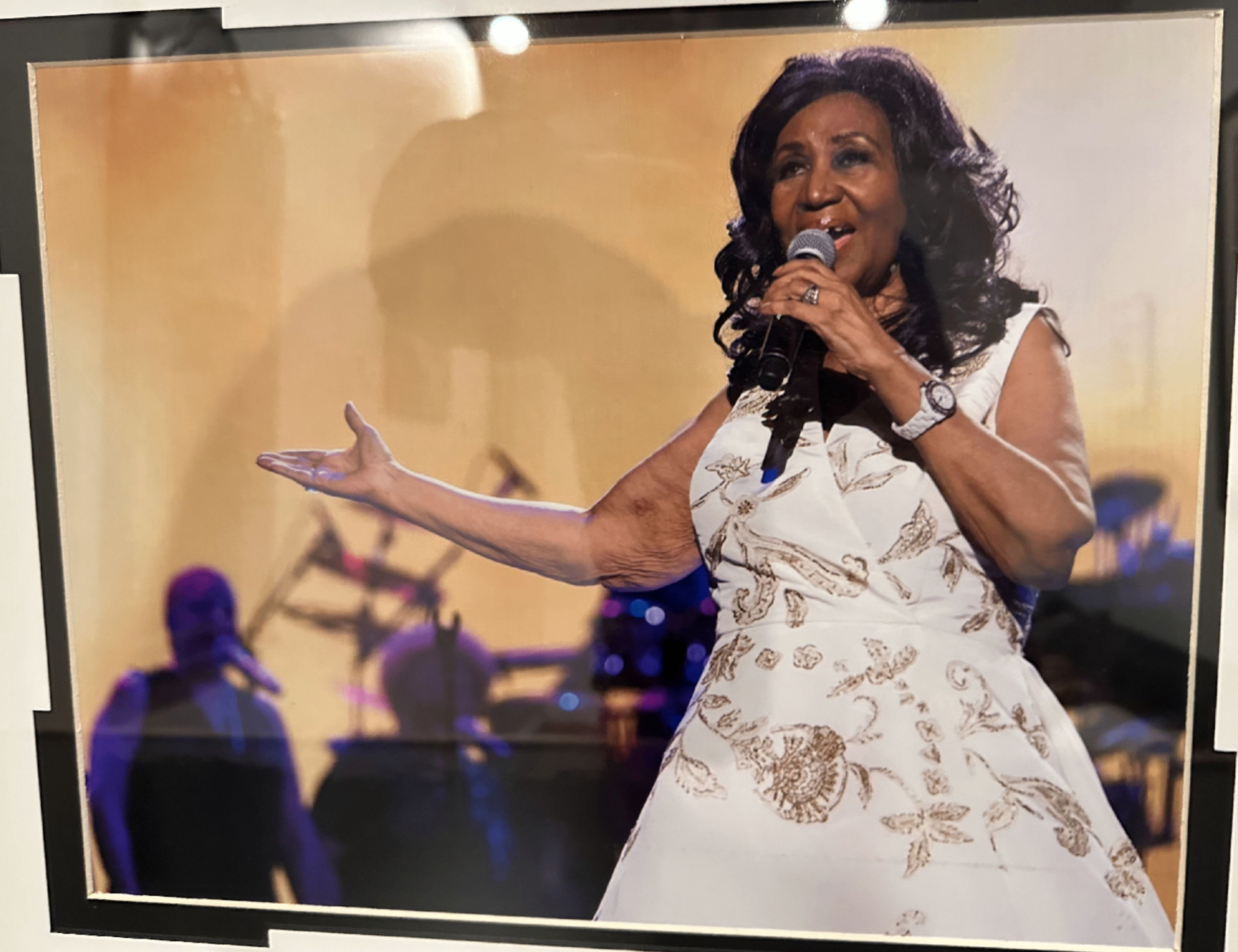Framed photograph of Aretha Franklin singing on stage in a white floral dress, sitting on the counter in the Rick James room.