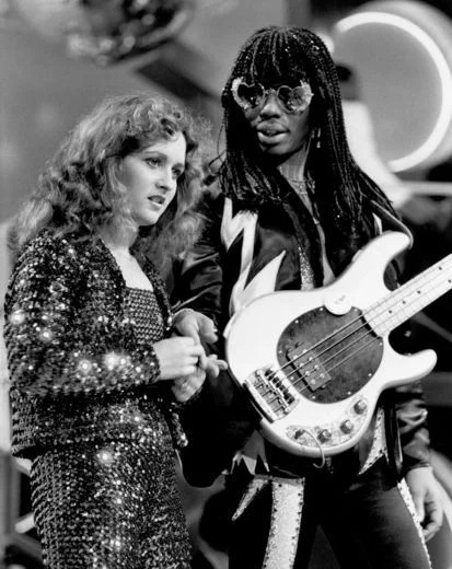 Black-and-white photo of Rick James and Teena Marie performing live in 1981, James holding a white bass guitar.