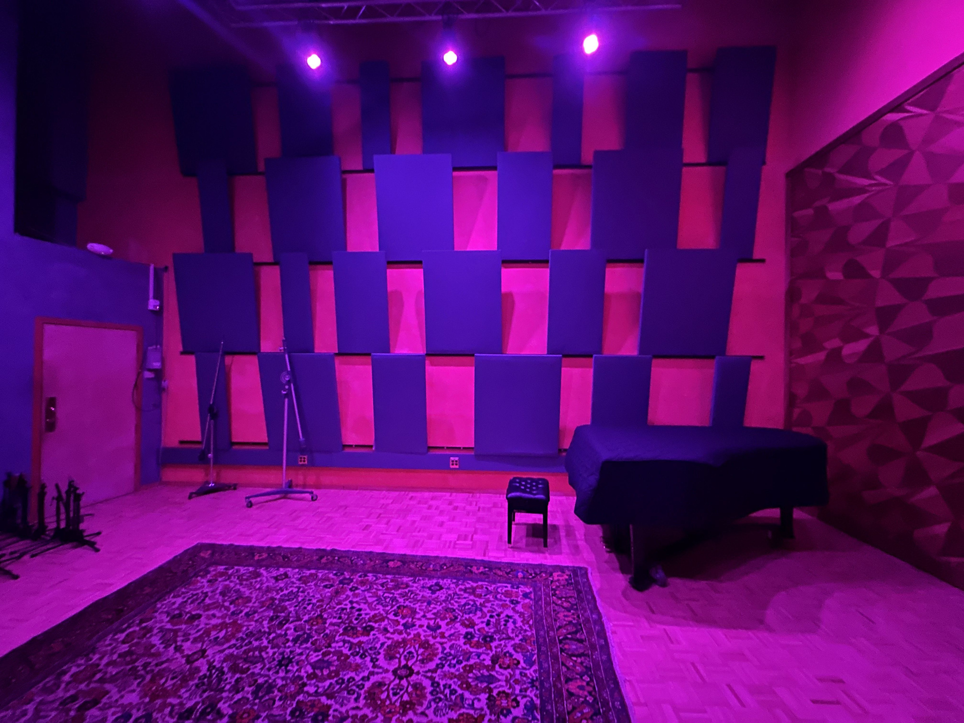 Studio A live room — staggered acoustic panels rising the full height of the wall, with the C7 and Persian rug on the parquet floor.
