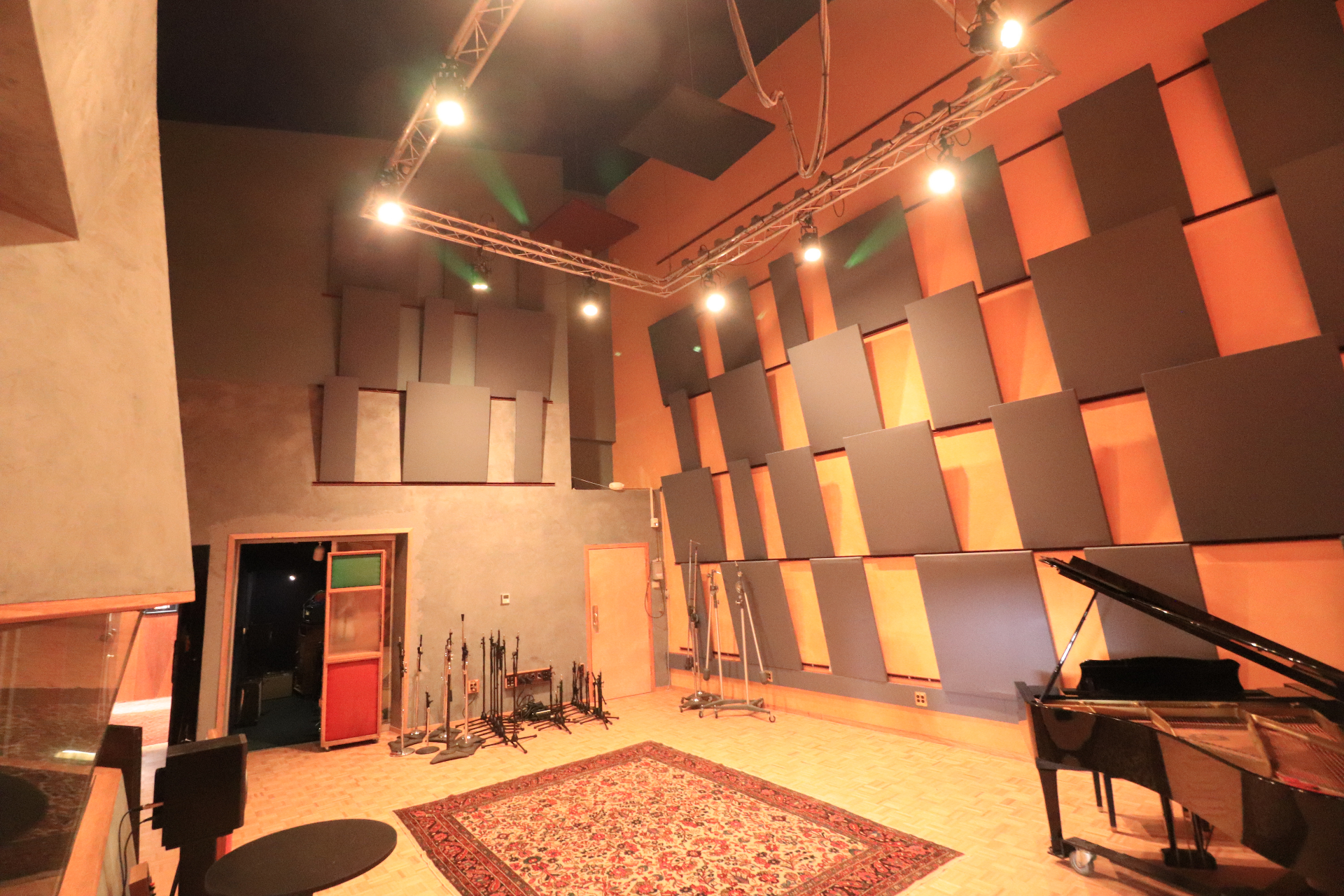 Studio A live room — full view facing away from the sunburst wall, showing the C7, Persian rug, mic stands, and acoustic panels climbing toward the 32-foot ceiling.