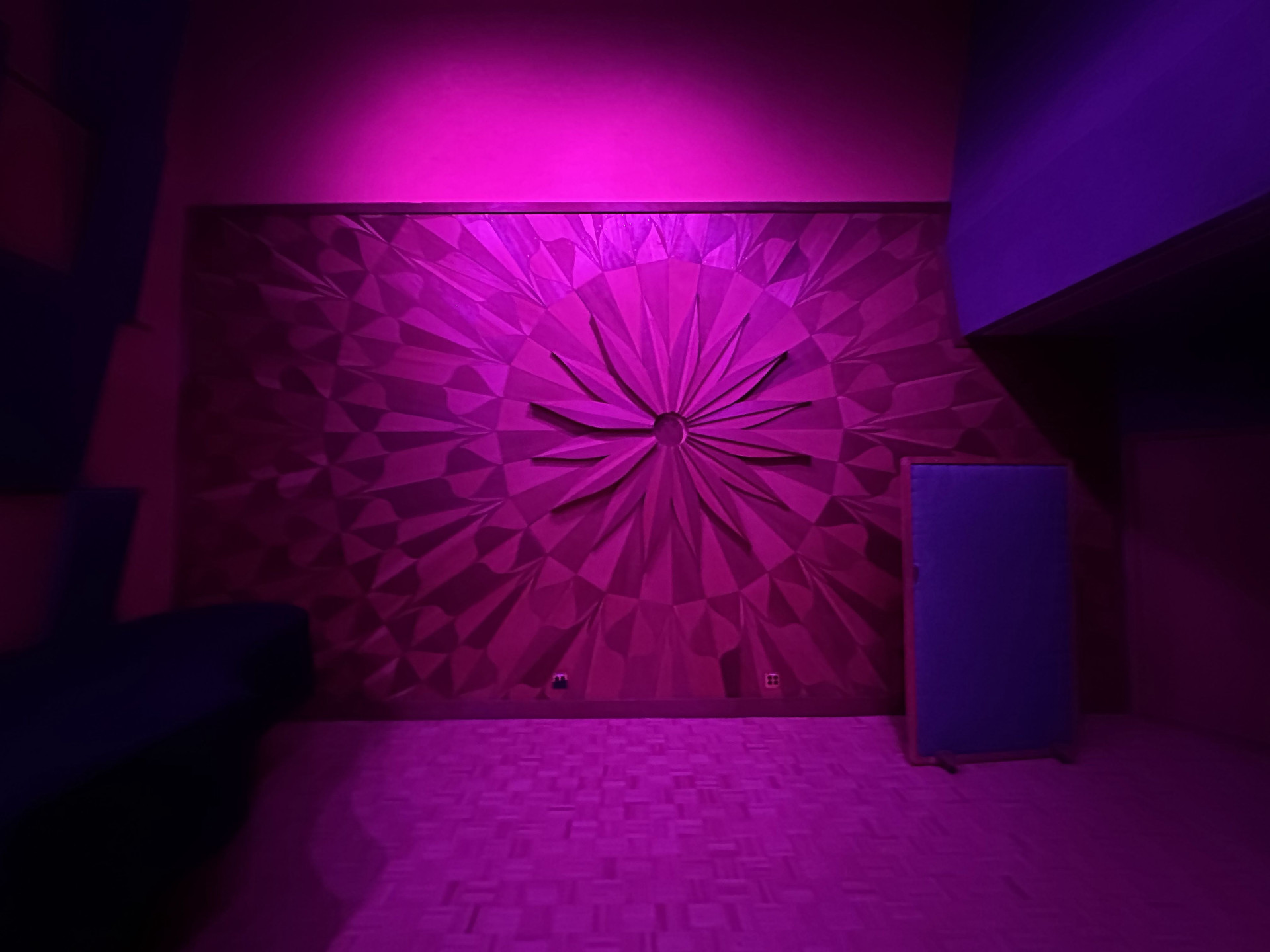 Carved wooden sunburst diffuser panel on the Studio A wall, lit in magenta.