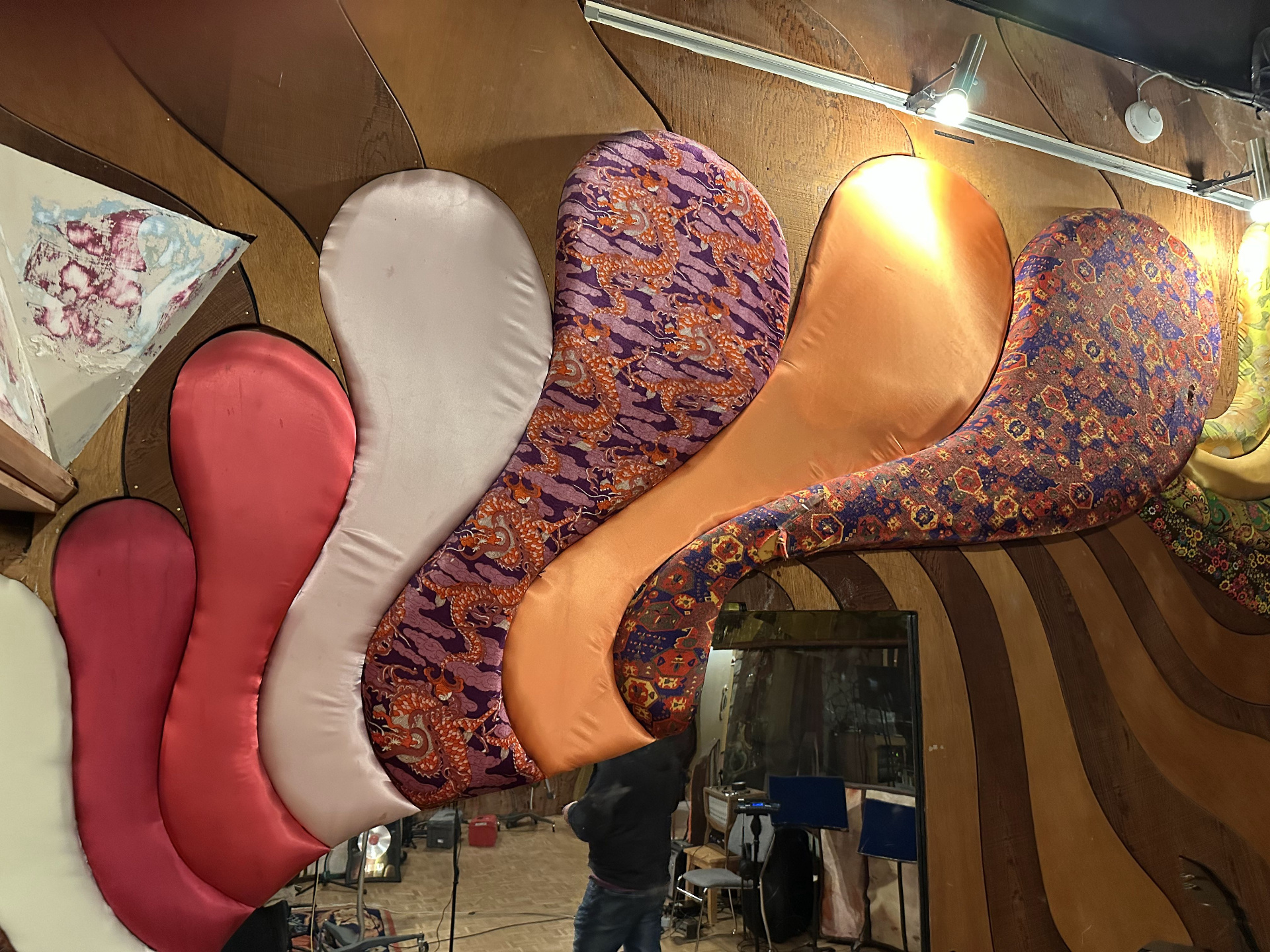 Curved cloud-shaped fabric panels covering the Studio B ceiling — coral satin, blush, orange dragon brocade, copper, and patterned tapestries on a redwood backing.