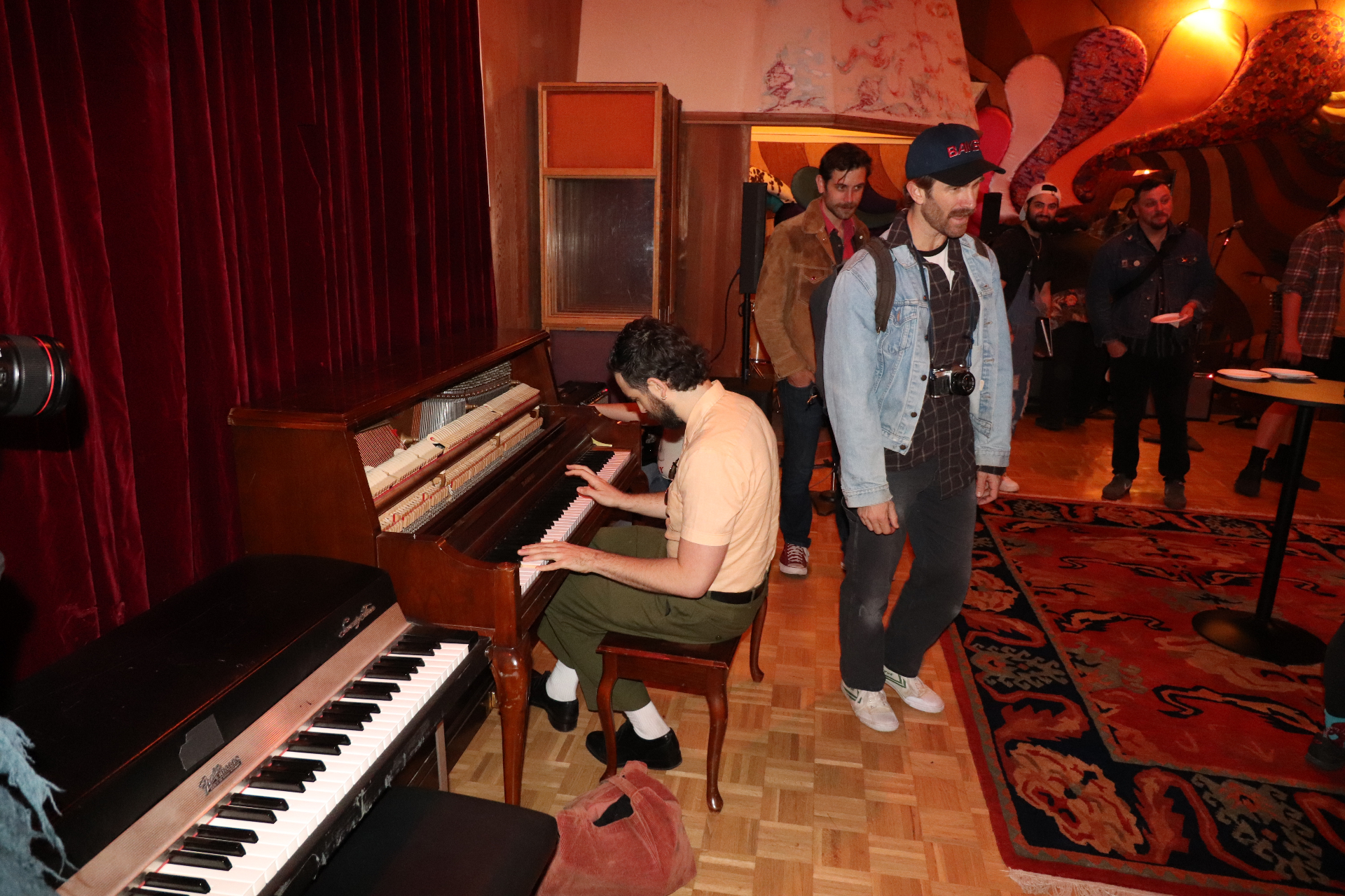 A pianist plays the Baldwin upright in Studio B during the Stereophonic cast party, with guests gathered on the Persian rug under the cloud ceiling.