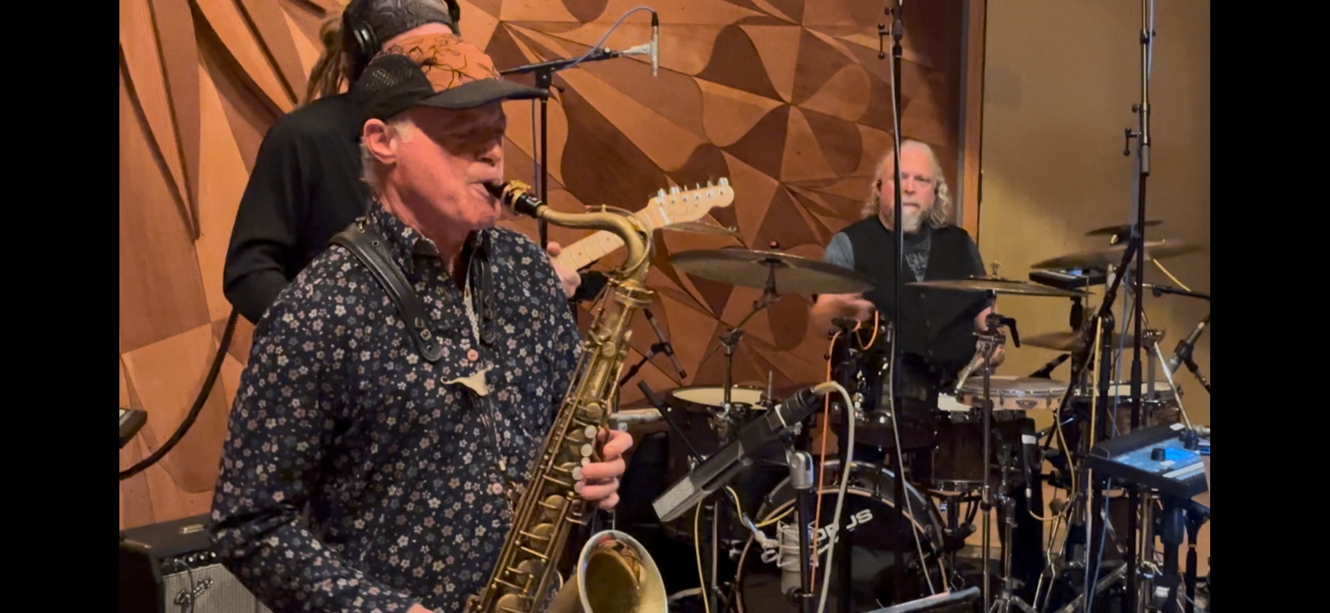 Lincoln Adler on saxophone in the foreground with Chris Gamper on drums behind him, tracking in Studio A against the carved wooden diffuser wall.