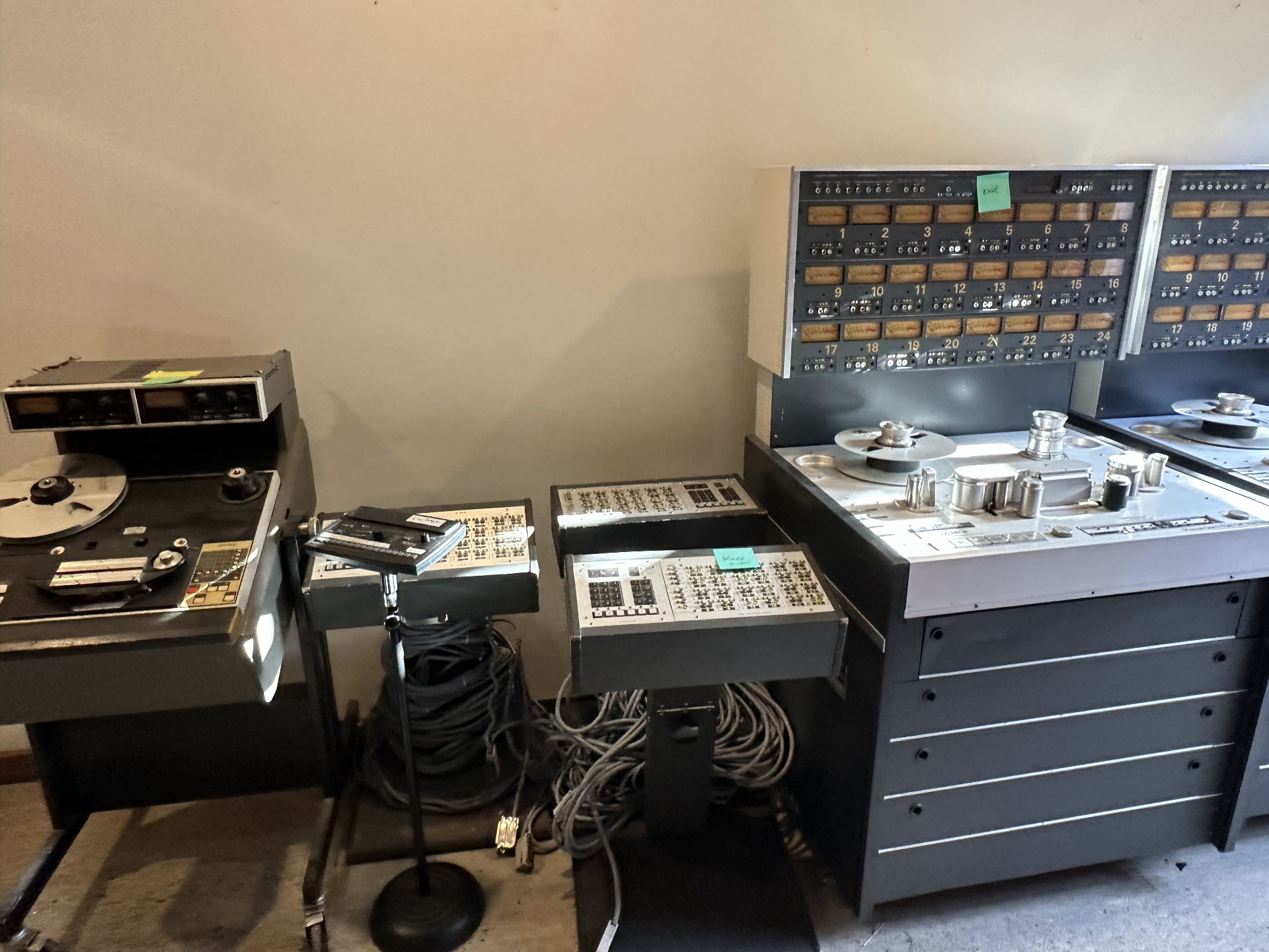 A pair of Studer 24-track tape machines pushed against a back-room wall, remote autolocators on stands, coiled cables on the floor, and the iconic numbered VU meter bridges glowing above the transports.