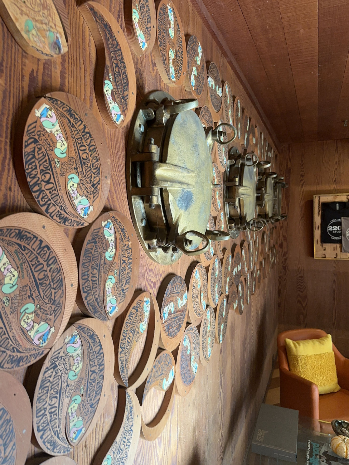 Angled close-up of the wall of carved redwood Halloween masquerade invitations clustered around a brass ship porthole.