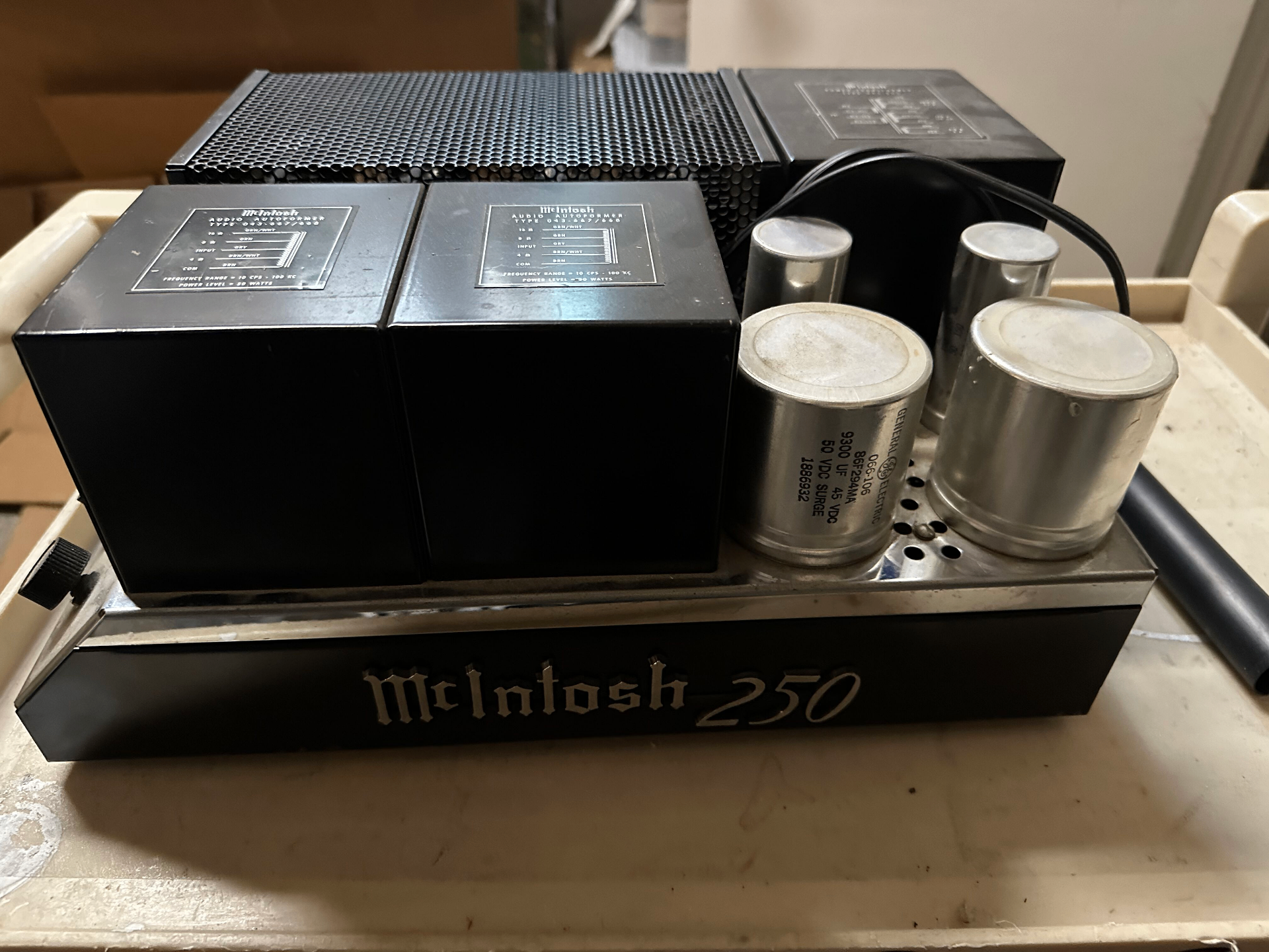 A vintage McIntosh MC250 solid-state power amplifier with its chrome top exposed, showing the twin black audio autoformers and four large General Electric capacitors.