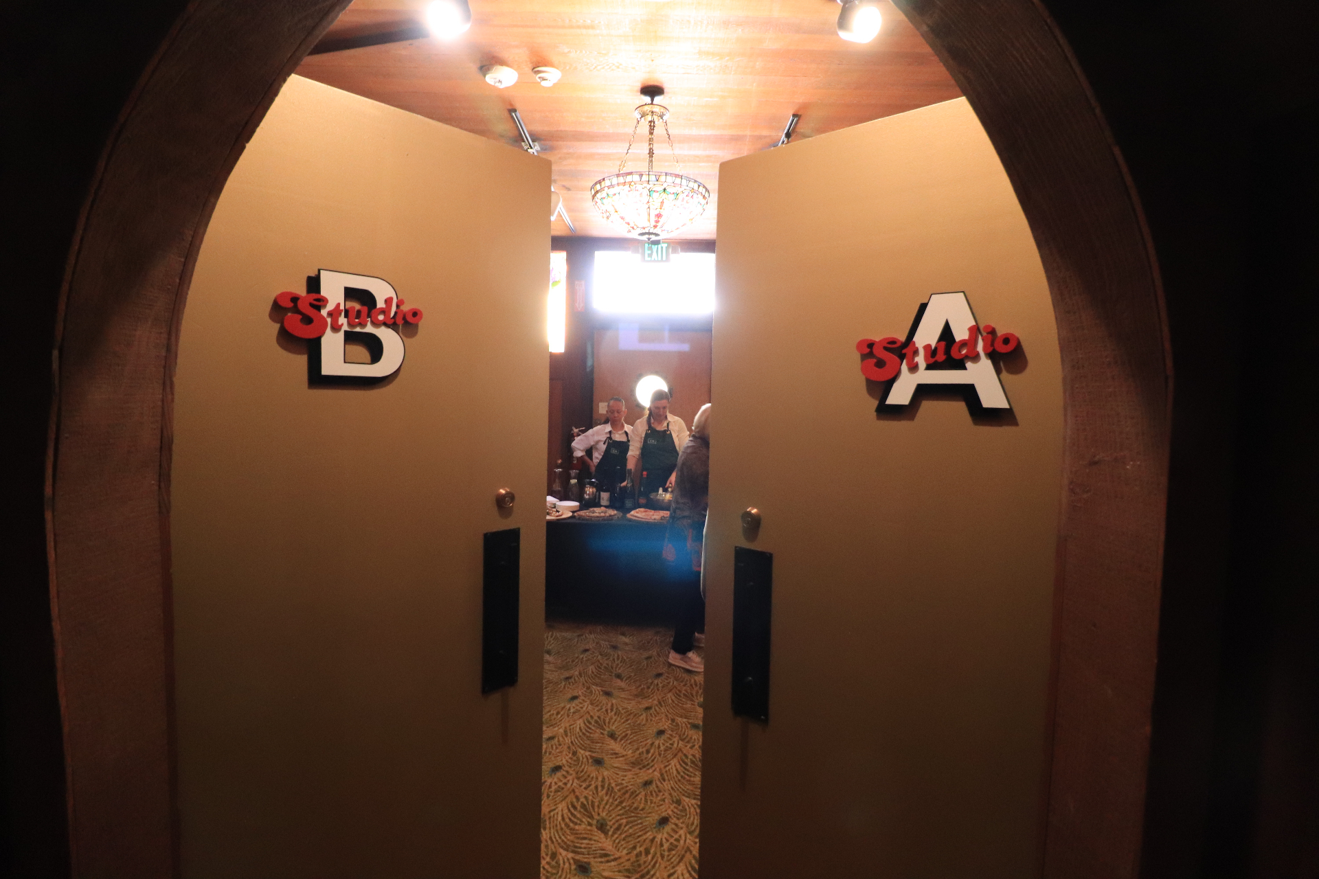 The arched doorway entrance to Studios A and B at 2200 Bridgeway — red 'Studio' script on white block letters mounted on twin doors, with a stained-glass chandelier and warm redwood ceiling beyond.