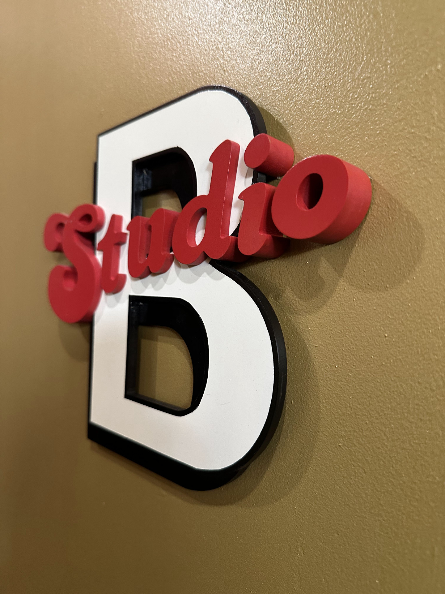 Hand-painted Studio B sign — white block 'B' with red script 'Studio' mounted on a gold wall.